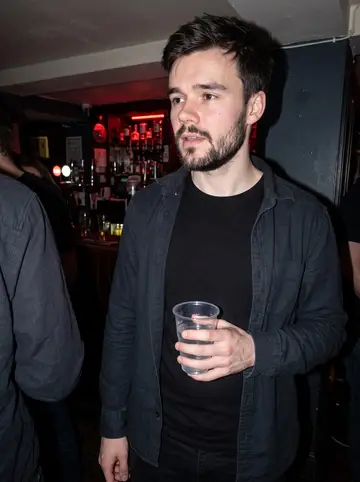 Orlando, AI character: a small Brighton pub after a loud metal night, black walls, crowded bar behind him