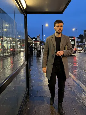 Orlando, AI character: outside Brighton station after an evening class, wet pavement and bus shelter glass behind him