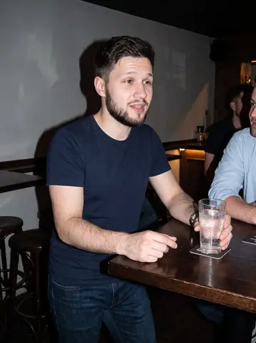 Julius, AI character: a low-key Worcester bar after work, standing near a high table with two coworkers partly cropped out of frame