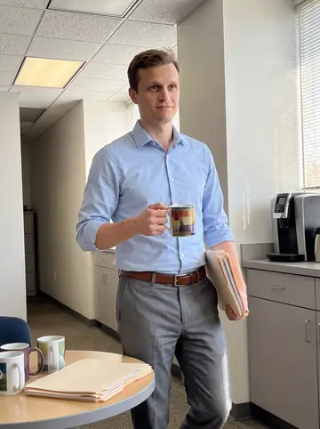Campbell, AI character: the break area at his Cleveland payroll office, walking past a small table with coffee mugs and a stack of…