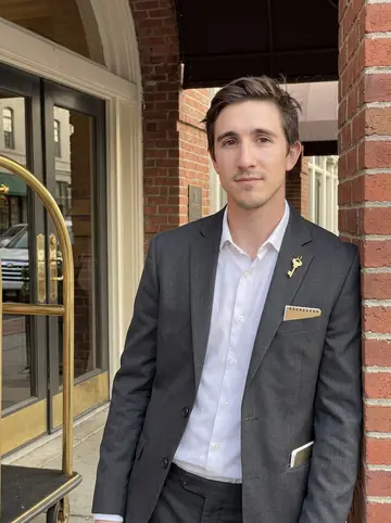 Alec, AI character: outside a historic Savannah hotel entrance after an early evening shift, leaning by a brick column near…