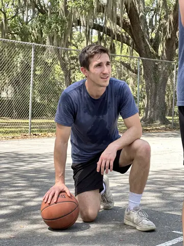 Alec, AI character: Sunday morning pickup basketball at a public court near a Savannah park, chain-link fence and oak trees in…