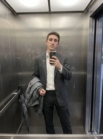 Alec, AI character: hotel service elevator at dusk after rain, stainless steel walls and a damp umbrella leaning in the corner