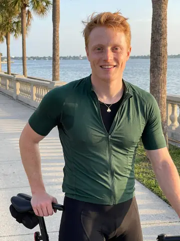 Shaun, AI character: Bayshore sidewalk in Tampa after an early evening bike ride, water and palm trees behind him
