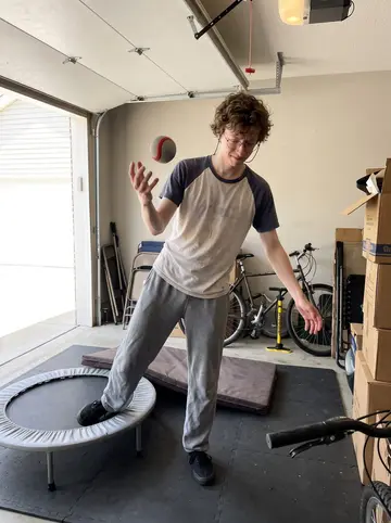 Melvin, AI character: his roommate's garage with a small trampoline on rubber mats, boxes and a bicycle stacked against the wall