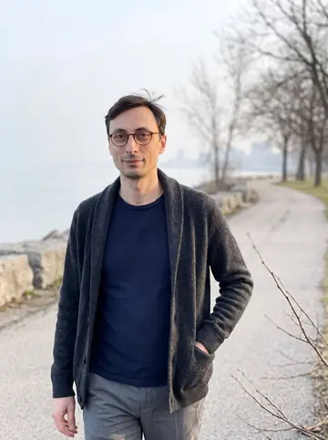 Dmytro, AI character: the Lake Erie shore path in Cleveland just after sunrise, pale fog over the water and bare trees behind him