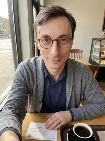 Dmytro, AI character: a quiet Cleveland cafe table near the window, a stamped postcard chess move and black coffee beside his elbow