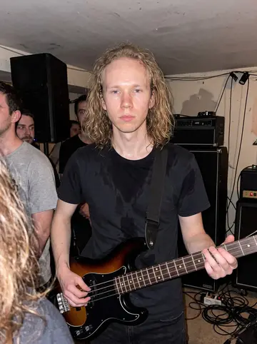 Johannes, AI character: tiny South Philly basement show after midnight, low ceiling, amp stacks, cables, and a few friends cropped…