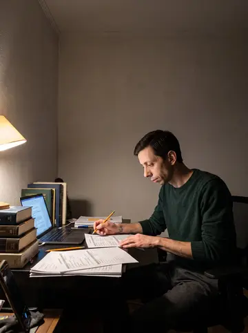 Eivind, AI character: his apartment desk with old city budget books, a laptop, pencil marks, and a small stack of rehearsal notes