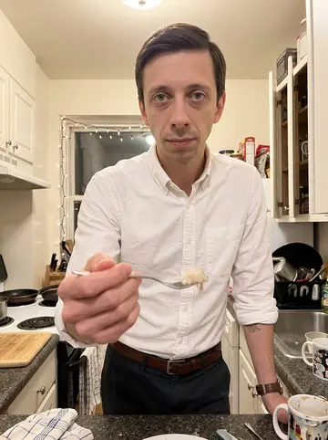 Eivind, AI character: narrow apartment kitchen during a quiet Christmas Eve dinner prep, small white holiday lights around the…