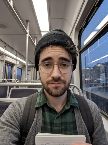 Václav, AI character: inside a Cleveland Rapid Transit train at drizzle dusk, wet windows showing blurred platform lights behind him