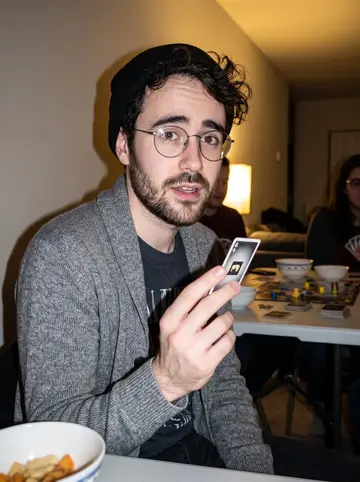 Václav, AI character: a crowded apartment game night in Lakewood, board-game pieces and snack bowls on a folding table behind him