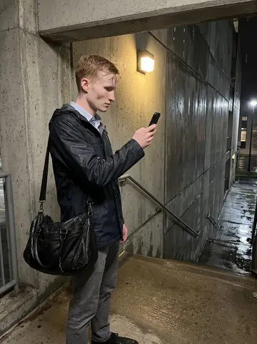 Lukáš, AI character: wet concrete stairwell outside a municipal parking garage in downtown Allentown while he photographs…