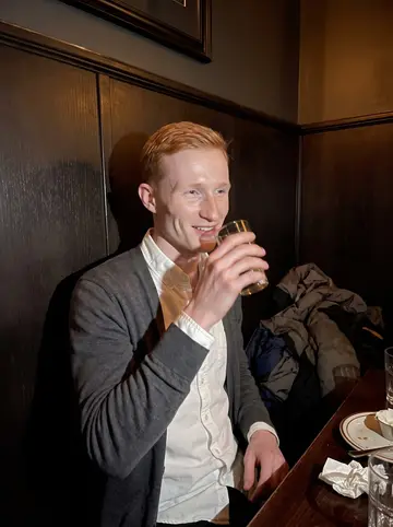 Lukáš, AI character: narrow booth at a neighborhood bar after a ballroom social, coats piled on the bench beside him