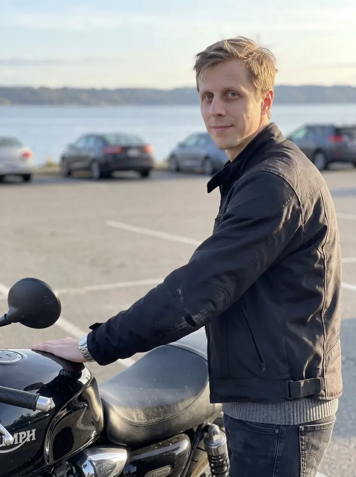 Aleksi, AI character: a quiet Seattle overlook parking pullout near Lake Washington after a ride, standing beside his old black…