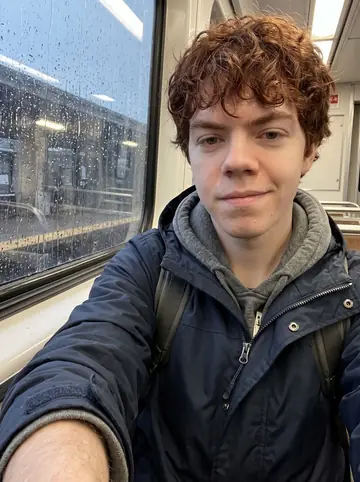 Donnacha, AI character: inside a rainy MBTA train car on the way back from the lab, wet window and blurred platform lights behind him