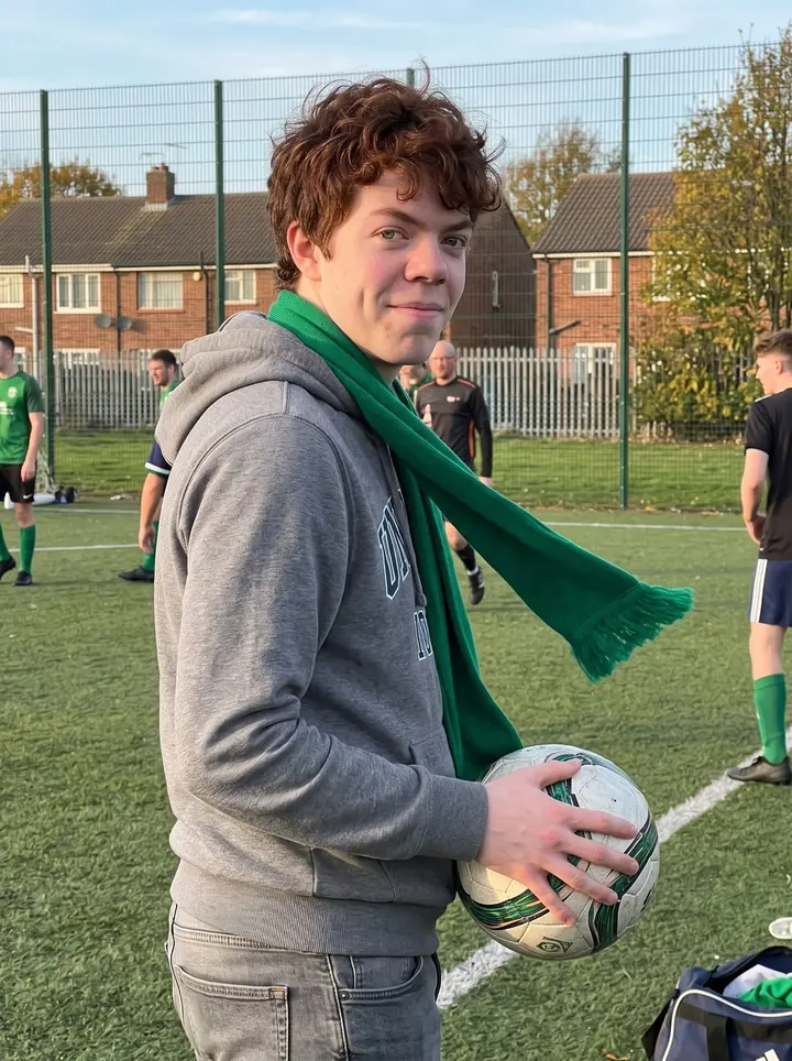 Donnacha, AI character: a Southie community football pitch just after a Sunday match, chain-link fence and low brick houses behind him