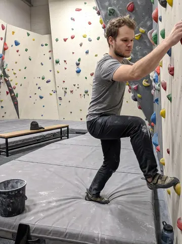 Fabian, AI character: the bouldering gym near his apartment on a wet winter night, phone propped low on a chalk bucket beside…