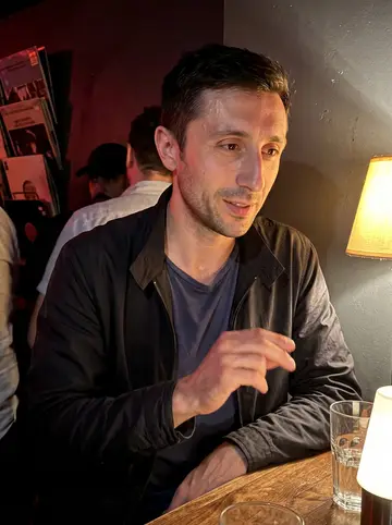 Anatoly, AI character: a small Brooklyn bar during an 1980s Soviet underground vinyl night, record sleeves stacked near the wall