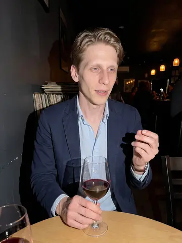 Rune, AI character: a crowded basement jazz bar in southeast Portland, standing near a small round table with records stacked…