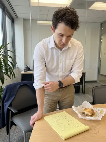Veljko, AI character: the small break area at his law firm, with a glass wall, office plants, and a cluttered lunch table
