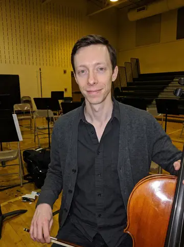 Vidar, AI character: a school gym after community orchestra rehearsal, folding chairs and music stands behind him