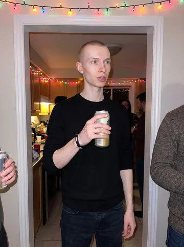 Jukka, AI character: a small Oshawa house party in December, standing near a kitchen doorway with colored holiday lights and…