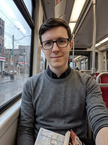 Petar, AI character: inside a Toronto streetcar on a rainy morning, wet window glass and blurred city blocks behind him