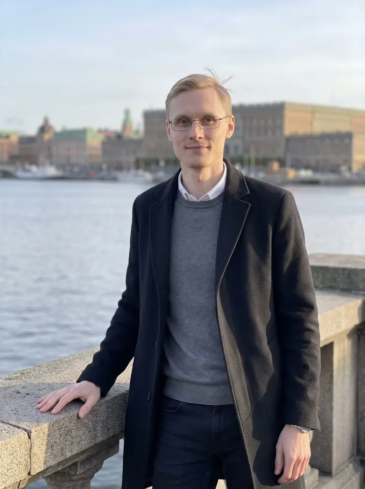 Oliver, AI character: Stockholm waterfront near Strömkajen after work, pale autumn sun on the buildings and water behind him