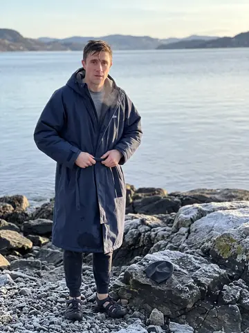 Øyvind, AI character: a rocky Oslofjord beach at six in the morning, winter water behind him and frost on the dark stones