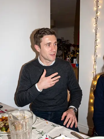 Øyvind, AI character: a warm family holiday dinner in a small Oslo apartment, blurred relatives and soft string lights behind him