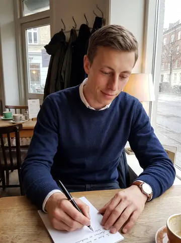Nicolai, AI character: a small quiet cafe near Nørrebro on a rainy spring afternoon, window glass dotted with rain