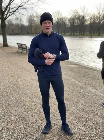 Antti, AI character: beside the Serpentine in Hyde Park after an ice swim, bare winter trees and grey water behind him