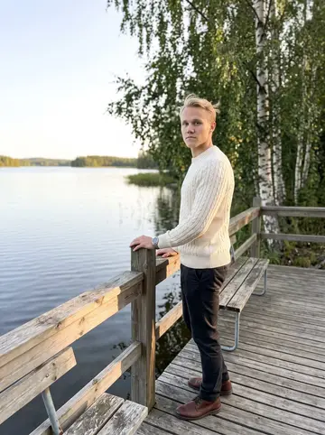 Antti, AI character: a wooden lakeside jetty in Finland during a short trip home, birch trees and still water behind him