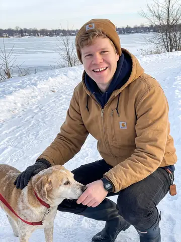 Martin, AI character: a snowy path beside Lake Harriet in Minneapolis, crouched next to Mabel after a dog walk, bare winter…