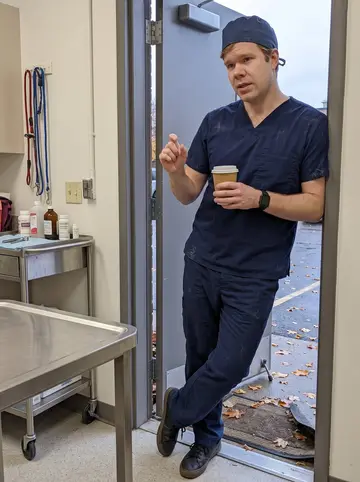 Martin, AI character: the staff side door of a small Minneapolis veterinary clinic during a short break, metal exam table and…