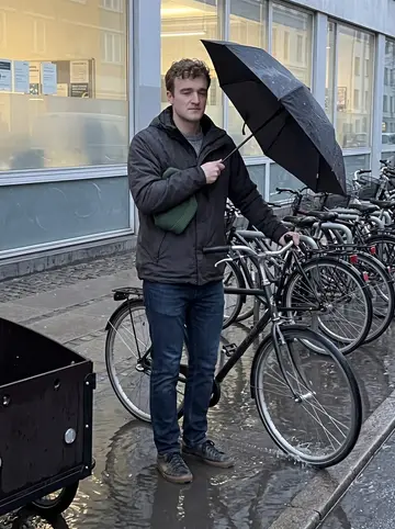 Søren, AI character: outside his supply planning office near a wet Copenhagen bike rack at the end of a rainy workday