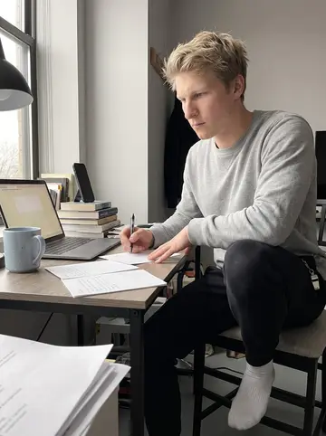Theodor, AI character: his small Chicago apartment desk on an overcast autumn afternoon, laptop open beside a stack of blank vow…