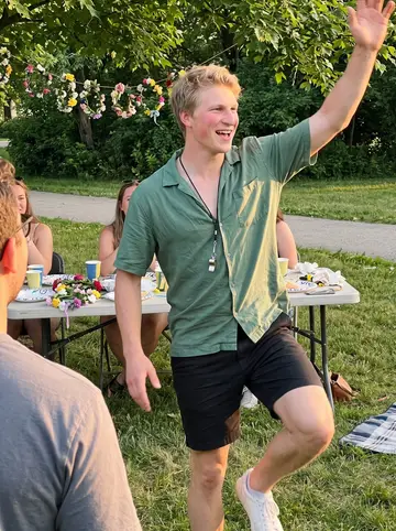 Theodor, AI character: a Swedish midsummer picnic in a Chicago park, paper plates and flower crowns on a folding table behind him