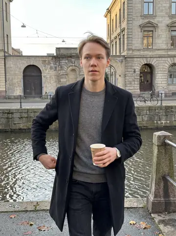 Hampus, AI character: beside a quiet canal in central Gothenburg after work, old stone buildings and tram wires behind him
