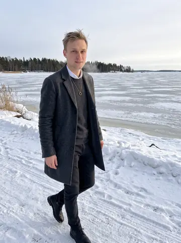 Sami, AI character: the frozen edge of the Oulu coast on a clear winter afternoon, low sea ice behind him and dark pine trees…