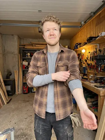 Lauri, AI character: his uncle's garage workshop on a Saturday, cedar sauna benches half assembled, pine boards stacked against…
