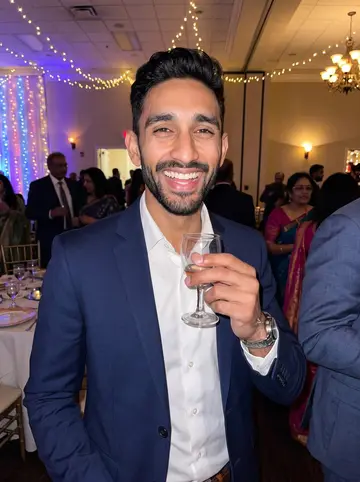 Yash, AI character: his cousin's wedding reception hall in Edison, adults in suits and saris blurred behind him