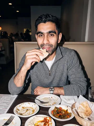 Fadi, AI character: a casual Lebanese restaurant in Dearborn after Saturday legal clinic, crowded table with small plates and…