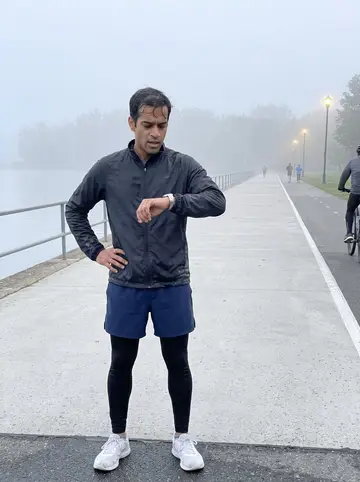 Umar, AI character: the lakefront running path just after dawn, pale water and a few other runners in the distance