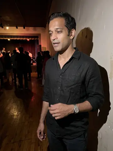Umar, AI character: a small South Asian community music night in Dearborn, stage lights and people behind him