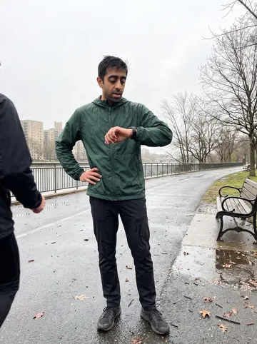 Deepak, AI character: a wet riverside running path in New Jersey after a light rain, apartment blocks and bare spring trees in…