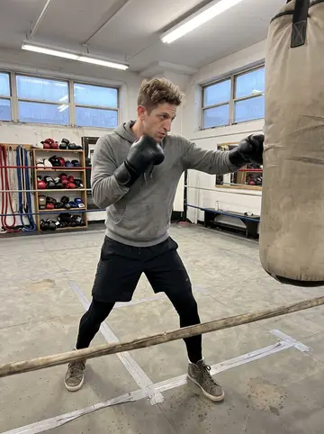 Patryk, AI character: a small boxing gym in Pilsen before sunrise, heavy bags and old ring ropes in the background