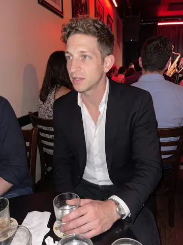 Patryk, AI character: a back room jazz bar in Wicker Park, crowded small table, brass instruments on the tiny stage behind him