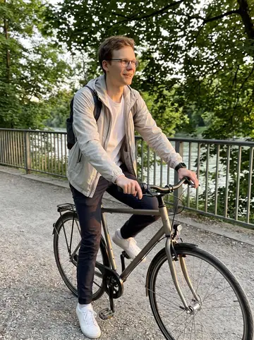 Timur, AI character: the Isar bike path on a Sunday evening, trees and river railings behind him